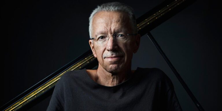 Colour portrait of Keith Jarrett in front of a piano, facing the camera.